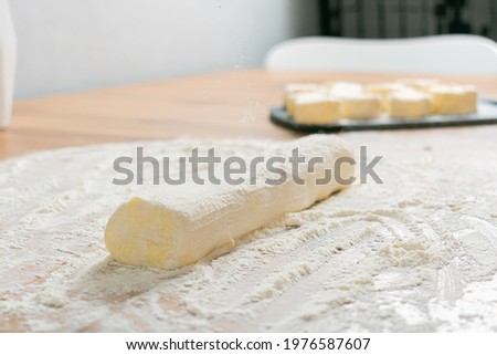 Woman's hands cutting homemade cinnamon roll dough over a floured surface with duster in background. Selective focus with blurred foreground and background