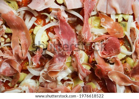 Top view on isolated uncooked raw homemade fresh prepared pizza with basic ingredients tomato sauce, onions, champignons, serrano and boiled ham