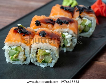 side view of juicy delicious rolls decorated with caviar. Japanese cuisine, black plate, close up