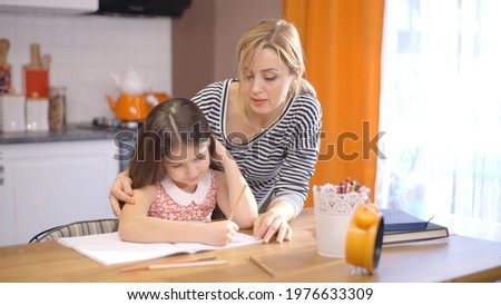 Child daughter 6-7 years old is studying with her young mother teacher. School kid girl teaching adult parent helping mom with studying homework sitting at desk at home. Children education concept..