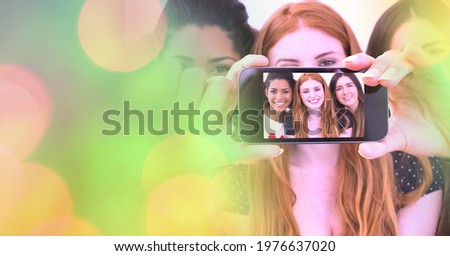 Composition of light circles over group of diverse female friends taking selfie with smartphone. global communication and social networking concept digitally generated image.