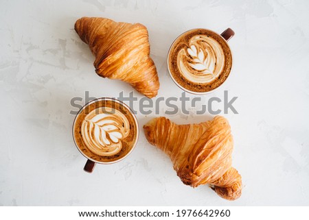 Flat lay of two cups of cappuccino and two croissant on white table Royalty-Free Stock Photo #1976642960
