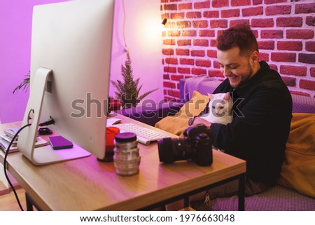 Man sitting at the sofa with his white cat at the laps and smiling happily