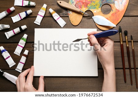 Man with spatula and blank canvas at wooden table, top view