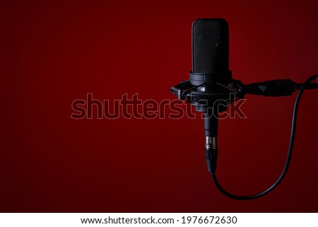 Black studio condenser microphone on red background, with copy space on left