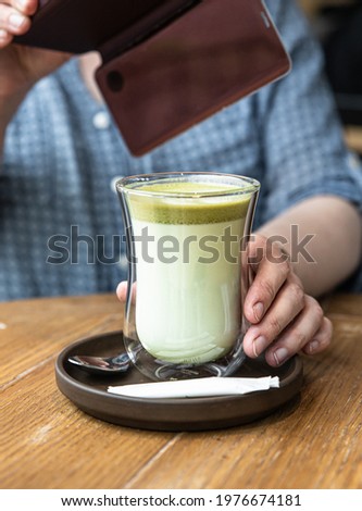 Woman holding her smartphone to shooting hot green tea matcha latte at cafe. Lifestyle concept. Selective focus.