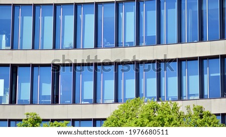 Modern downtown office building surrounded by greenery tree, the surface window outside reflecting clear blue sky. Business office building and green trees, business and nature concept. 