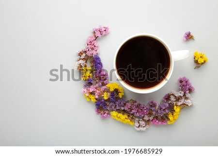 Cup of coffee with flowers on grey background. Flat lay, top view