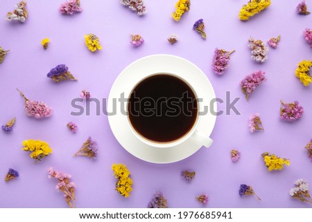 Cup of coffee with flowers on purple background. Flat lay, top view