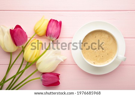 Cup of coffee with tulips on pink background with copy space. Top view