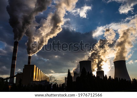 A view of the smoking chimneys of a coal-fired power plant against the backdrop of a dramatic sky with clouds. The photo was taken in natural daylight. Royalty-Free Stock Photo #1976712566