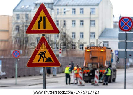 warning signs about street repairs on a blurred background with repair workers, close-up