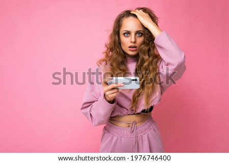 Photo of attractive crazy amazed surprised young woman wearing casual stylish clothes standing isolated over background with copy space holding and using mobile phone looking at camera