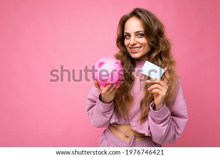 Portrait photo of happy positive smiling young beautiful attractive woman with wavy long blonde hair with sincere emotions wearing stylish pink hoodie isolated over pink background with copy space