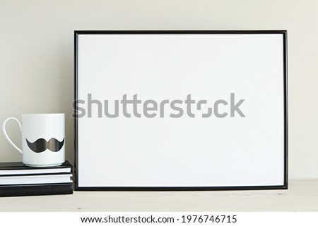 Black horizontal frame mockup for wall art presentation,  monochrome interior, hipster mug with mustache, books.