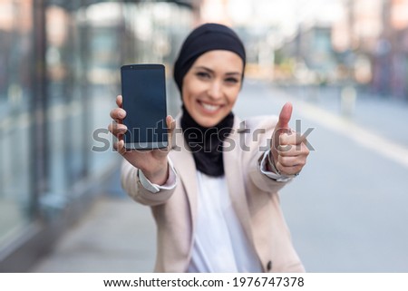 Arabic business woman holding phone and holding thumbs up closeup Royalty-Free Stock Photo #1976747378