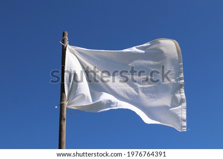 The white flag against the blue sky.  Surrender concept. Royalty-Free Stock Photo #1976764391