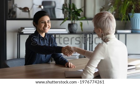 Smiling multiethnic businesswomen shake hands close deal or agreement at meeting in office. Happy young Indian woman handshake business partner get acquainted greet at briefing. Employment concept. Royalty-Free Stock Photo #1976774261