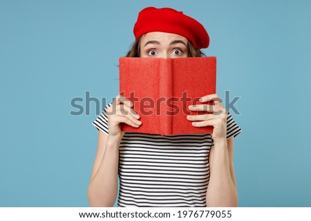Young smart student woman 20s with short hairdo wearing french beret red hat striped t-shirt hiding cover face mouth with diary read book novel isolated on pastel blue color background studio portrait Royalty-Free Stock Photo #1976779055