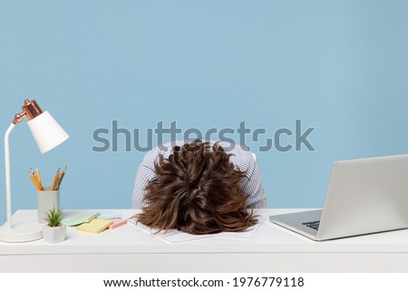 Young tired exhausted frustrated secretary employee business woman wearing casual shirt sit work sleep laid her head down on white office desk with pc laptop isolated on pastel blue background studio Royalty-Free Stock Photo #1976779118