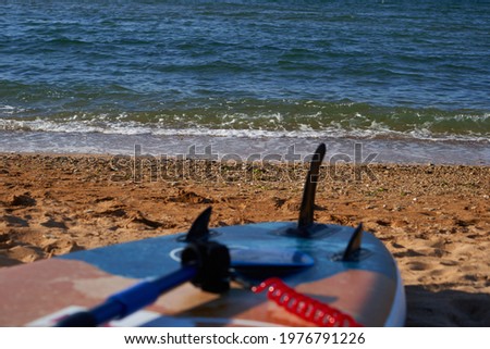 The SUP board and a paddle lies on the beach on the sand by the blue sea.                      