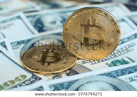 The gold bitcoin cryptocurrency coin stands on its own end, the second one lies on one hundred dollar bills