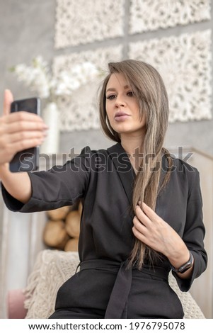 Stylish fashionable young woman trendy clothes posing taking selfie use smartphone at professional photo studio. Blonde female photographing on mobile phone at luxury vintage interior with spotlight