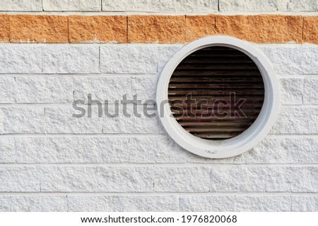 Rough cement block wall with gray and red colors with a circular air outlet on the right side. Architecture and design concept.