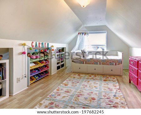 White vaulted ceiling kids room with hardwood floor and rug. Room furnished with single bed, pink antique dresser and  storage units for toys