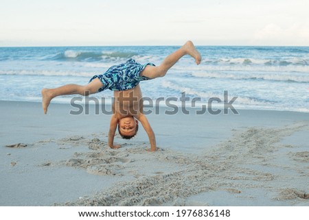 Boy doing a somersault on the sand on the beach. Exciting child having fun on the beach. Vacations by the sea. Outdoor activities with children. Summer swimming. Royalty-Free Stock Photo #1976836148