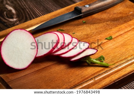                    Fresh red sliced radish on a wooden board with the knife on side.             