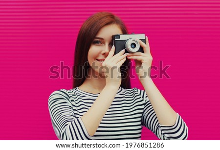 Portrait of young woman photographer with vintage film camera on a pink background