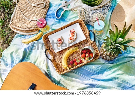 Summertime healthy picnic. Fresh tropical fruit, sweet stawberry sandwiches and refreshing drink in mason jar on wicker tray on blue cloth in the garden.