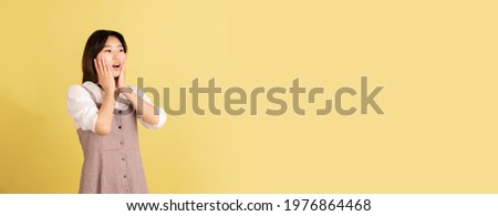Shocked, amazed, flyer. Asian young woman's portrait isolated on yellow studio background. Beautiful female model in casual style. Concept of human emotions, facial expression, youth, sales, ad.