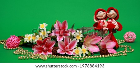 Spring flowers lilies. On a beautiful gentle green background. Souvenir red figurine of a fairy girl. Macro. Postcard with floral wallpaper. Romantic artistic image, place for text.