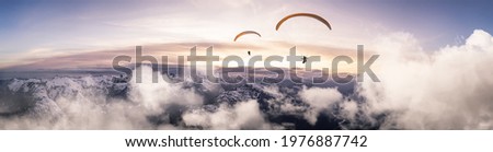 Adventure Composite Image of Paraglider Flying up high in the Rocky Mountains. Sunny Sunset Sky. Aerial Background from British Columbia, Canada. Extreme Sport Concept. Panorama Royalty-Free Stock Photo #1976887742