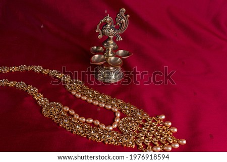 Indian traditional bronze oil lamp in the shape of a bird and gold Indian female jewelry on the red sari background. traditional Indian religious ceremony of Hindus. Diwali