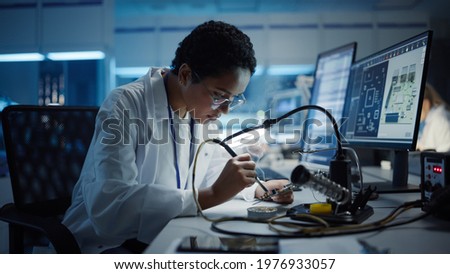 Modern Electronics Research, Development Facility: Black Female Engineer Does Computer Motherboard Soldering. Scientists Design PCB, Silicon Microchips, Semiconductors. Medium Close-up Shot Royalty-Free Stock Photo #1976933057