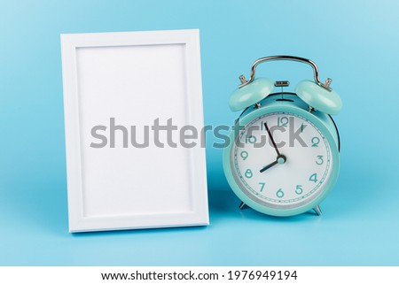 Vintage alarm clock and white photo frame on blue with copy space. 