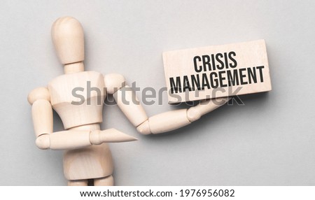 Wooden man shows with a hand to white board with text crisis management,concept