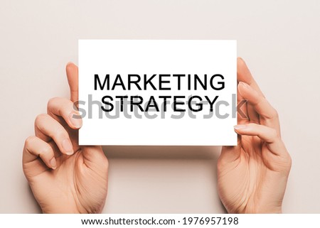 Female hands hold card paper with text Marketing Strategy on a yellow background. Business and finance concept