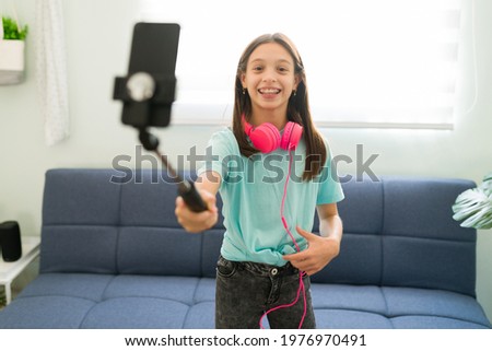 Portrait of a beautiful young girl smiling while taking a selfie with her smartphone. Kid influencer recording a video at home