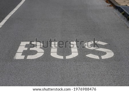 Selective focus of white BUS letter on black grey asphalt street in countryside, Bus lane road in front of station.