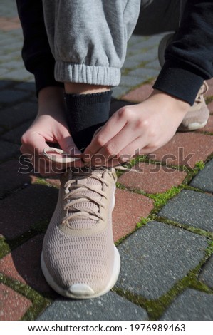 A person tying the laces of a beige sports shoe while walking outdoors