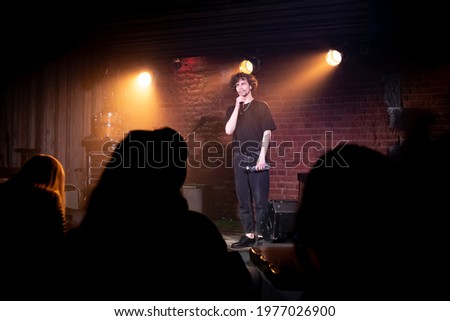 Young Caucasian male comedian performing his stand-up monologue on a stage of a small venue Royalty-Free Stock Photo #1977026900