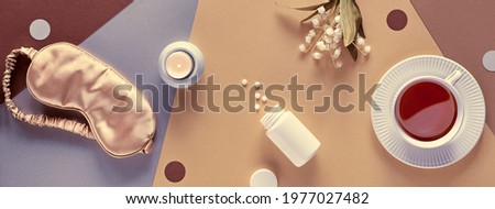 Quality of sleep banner. Sleep mask, sleeping pills, scented candle and cup of calming tea. Two tone layered silver, gold, beige and brown paper flat lay, top view. Lily of the valley flowers.