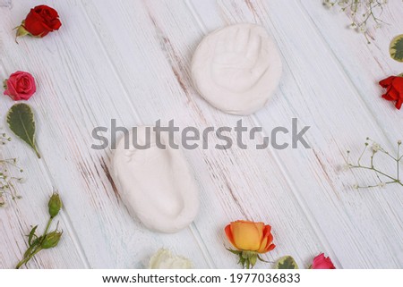 Baby hand and foot print on plaster on wooden background, flat lay with flower