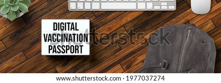 lightbox with message DIGITAL VACCINATION PASSPORT and a backpack on wooden background