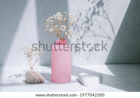 Trendy interior composition with sunlight and shadows. Gypsum geometric shapes, natural stone, decorative pink vase and gypsophila flowers on a white gray background.
