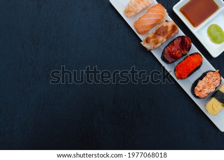 The sushi set is a famous Japanese dish, put on a ceramic plate, beautifully arranged on a black background.